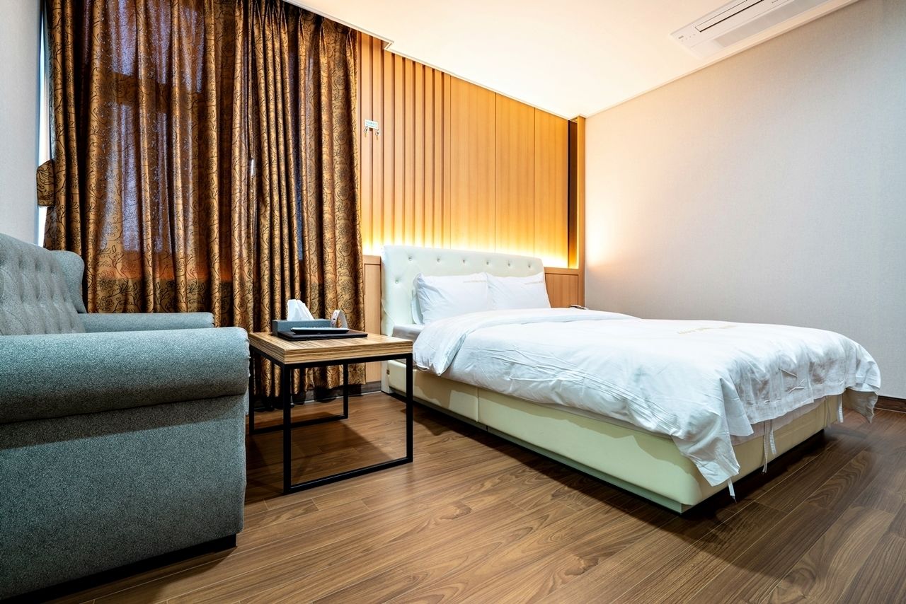 Une chambre d’hôtel avec un lit, une chaise, une table de chevet et une grande fenêtre avec des rideaux.