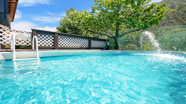 Une piscine d’un bleu éclatant, avec une terrasse en bois et un arbre en arrière-plan.