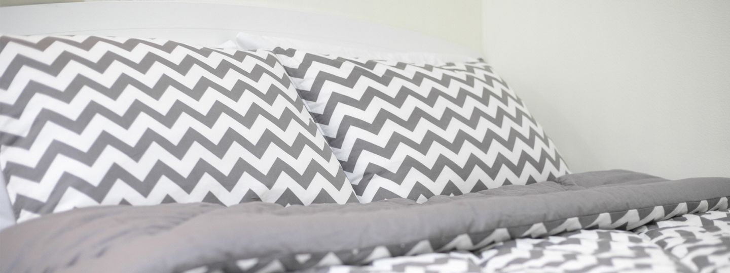 A bed with grey and white patterned bedding.