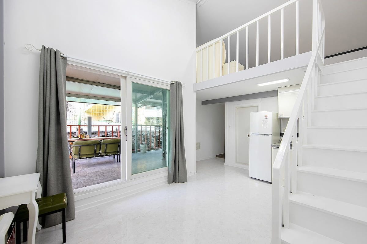 A spacious room with a large sliding glass door leading to an outdoor area, a white staircase, and a kitchenette.