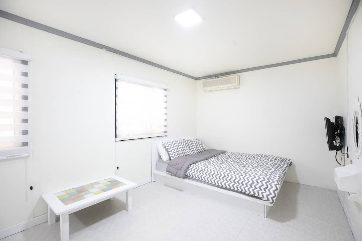 A small, clean room with a single bed, a bench, and a window.
