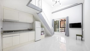 Une cuisine moderne avec des meubles blancs, un comptoir en granit et un four à micro-ondes encastré. Un escalier mène à un espace extérieur offrant une vue sur les arbres.