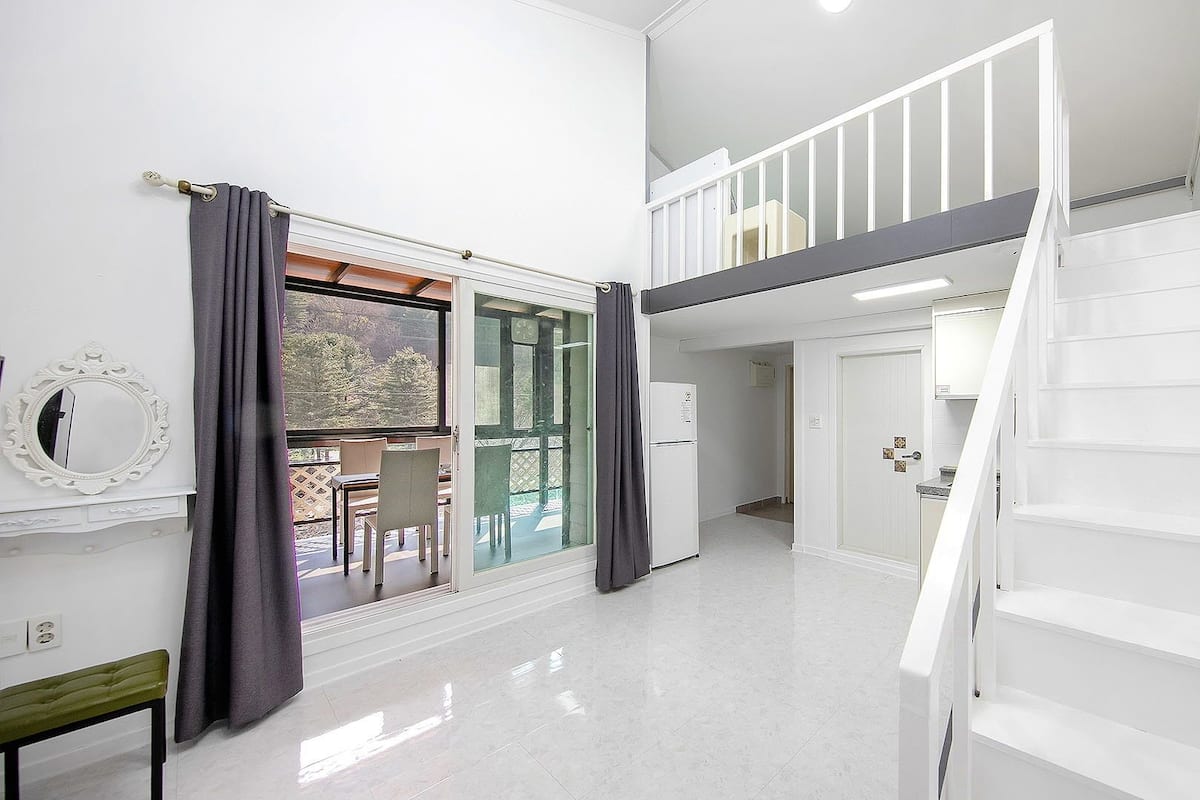 A spacious room with a white staircase, a dining area with a table and chairs, and a view through a glass door.
