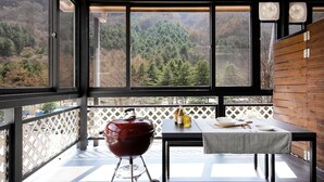 Un balcon avec un barbecue, une table et des bouteilles, donnant sur une zone boisée.