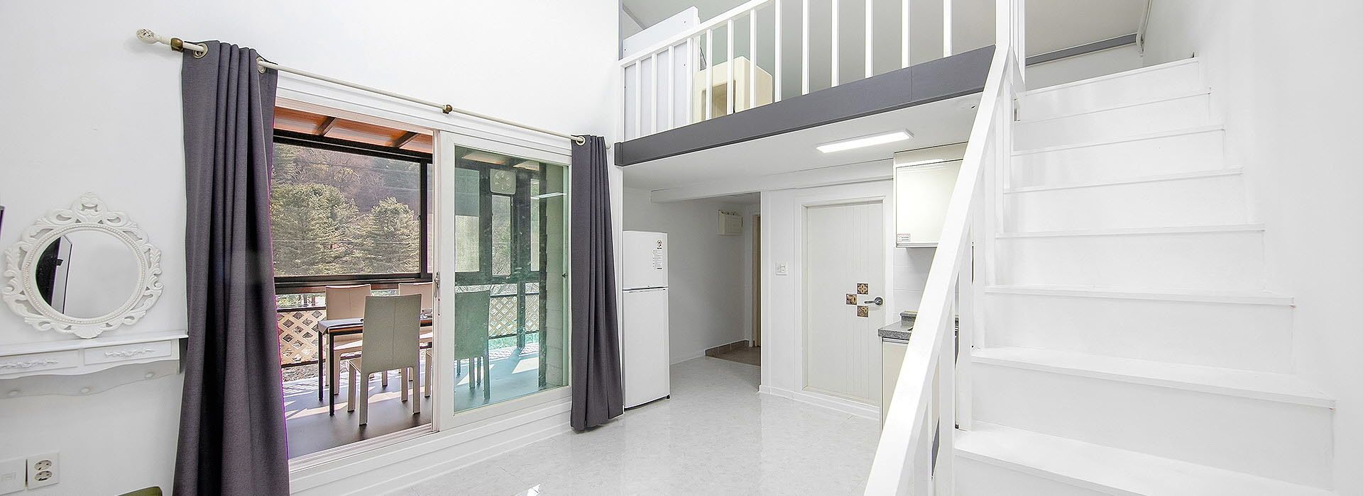 Un couloir donnant sur un espace repas, avec un escalier, et une vue sur l’extérieur.