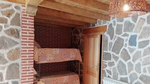A room with a stone wall, a wooden ceiling, and a bunk bed with a patterned bedspread.