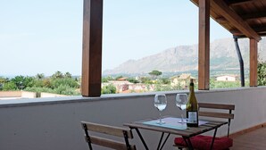 Taula de fusta amb dues copes de vi i una ampolla a un balcó amb vistes a un paisatge muntanyós.