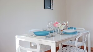 Taula de dinar blanca amb plats blaus i gots de vidre transparent, decorada amb flors blanques.