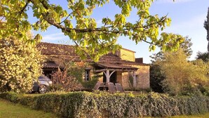 Una casa de pedra rústica amb teulada a màxima, envoltada per un bordatge ben cuidat i un cotxe estacionat al davant.