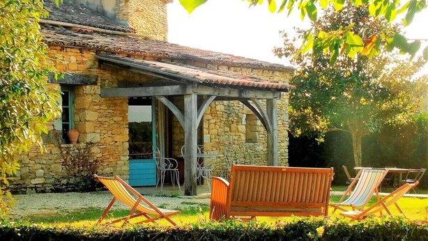 Una casa de pedra amb teulada de teules, un porxo cobert amb mobles de fusta i vista al jardí circumdant.