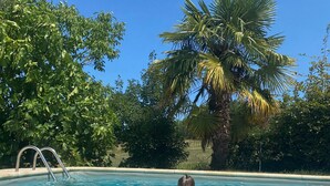 Una persona flotant sobre un flotador groc en una piscina blava cristal·lina, envoltada de vegetació abundant i una palmera.