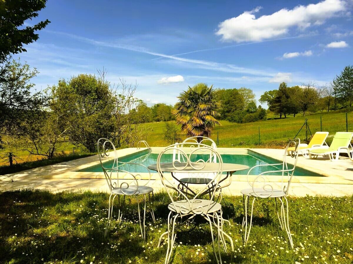 Zona de piscina con mesa y sillas, rodeada de follaje y árboles.