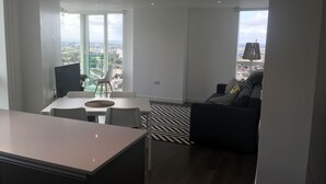 Una sala de estar moderna con un sofá negro, una mesa de comedor con sillas y un gran ventanal con vistas a la ciudad.