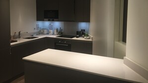 Una cocina moderna con gabinetes oscuros, encimera blanca e iluminación bajo los armarios.