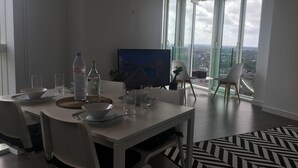Un comedor moderno con una mesa dispuesta para cuatro, un ventanal con vistas a la ciudad y un televisor de pantalla plana en la pared.