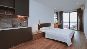 A modern hotel room with a kitchen area, a large bed, and a view of a body of water. - BH Riverside Hotel (Hanoi)