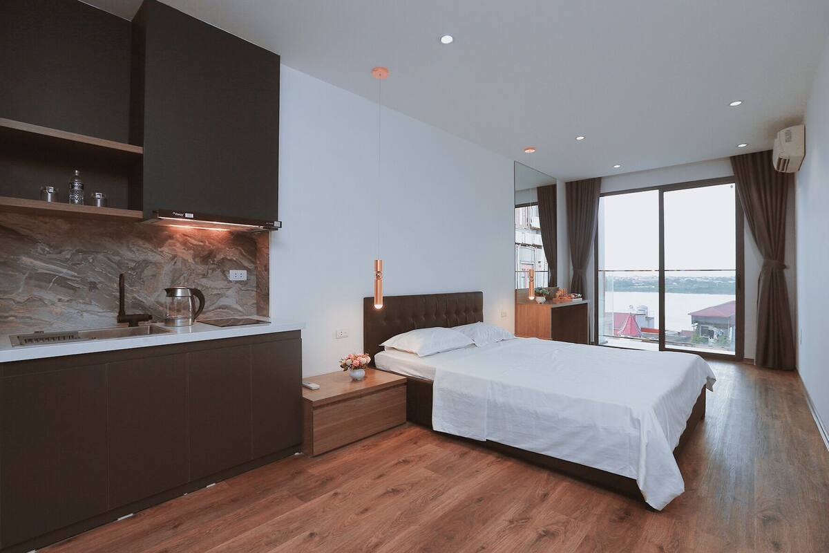 A modern hotel room with a kitchen area, a large bed, and a view of a body of water.