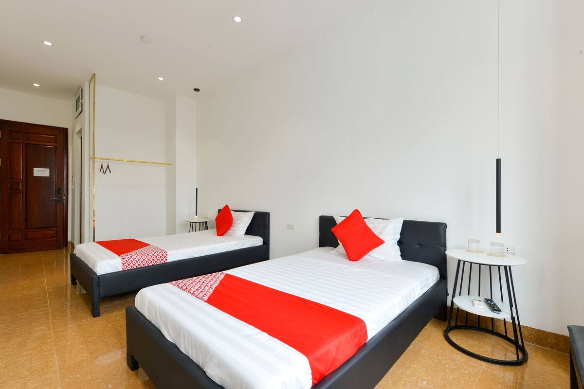 A hotel room with two beds, each with a red and white bedspread, a small round table with a remote control, and a wooden door.