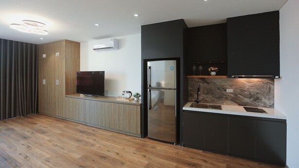 A modern kitchen with a wooden floor, a built-in TV, a refrigerator, and a black countertop. - BH Riverside Hotel (Hanoi)