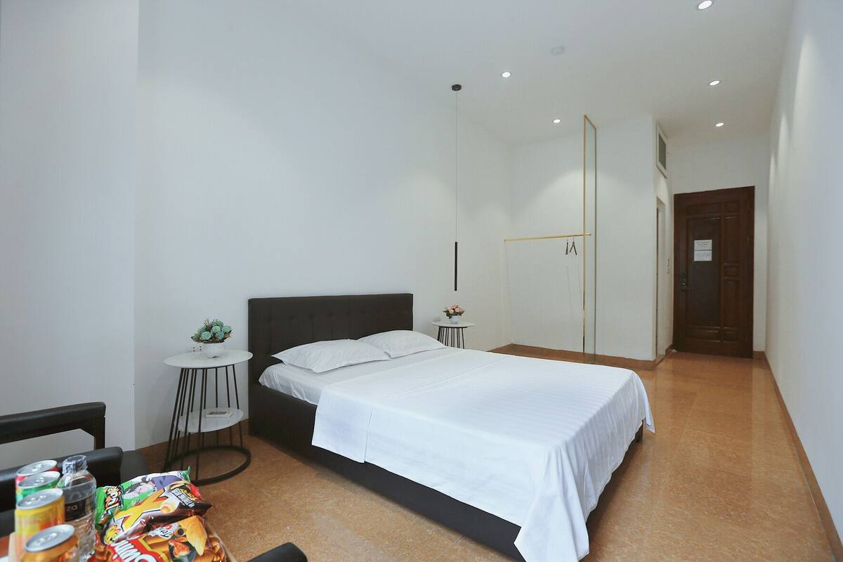 A modern bedroom with a large bed, a small round table with a vase, and a chair.