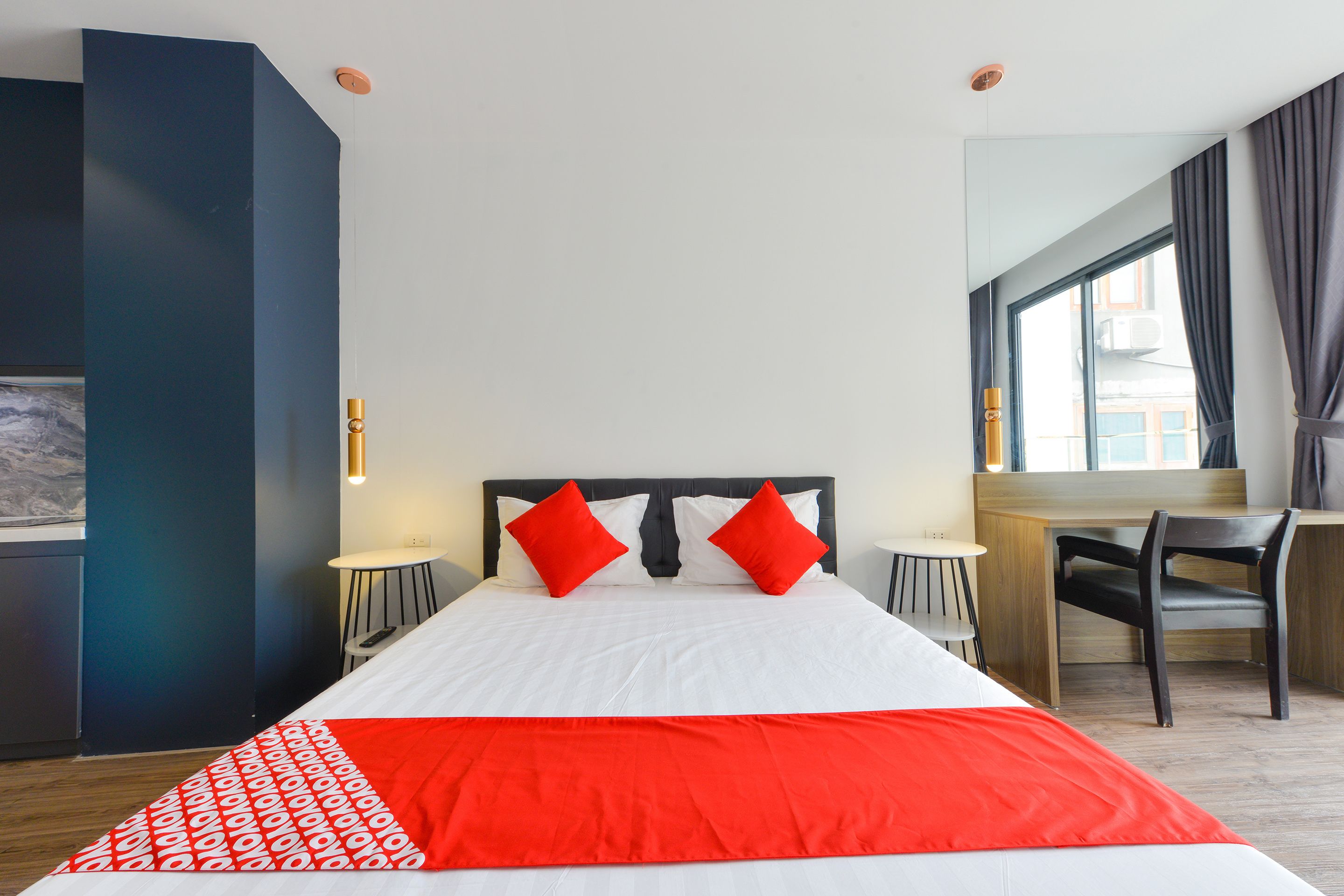 Quarto de hotel moderno com uma cama grande, roupa de cama vermelha e branca, uma escrivaninha e uma cadeira.