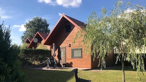 A rustic cabin with a sloped roof, a small porch, and a bird statue in the foreground. - House 3 - lakesearch on Labussee (Userin)