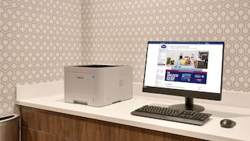Una impressora Samsung sobre un taulell blanc amb un monitor d'ordinador que mostra una pàgina de reserves d'hotel.