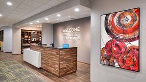 A hotel reception area with a wooden reception desk, a "Welcome to the Bee Hive State" sign, and a large abstract painting on the wall. - Hampton Inn Draper Salt Lake City Ut (Draper)