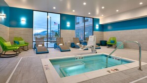 A modern indoor pool area with lounge chairs, a pool with depth markers, and large windows offering a view of the mountains. - Hampton Inn Draper Salt Lake City Ut (Draper)