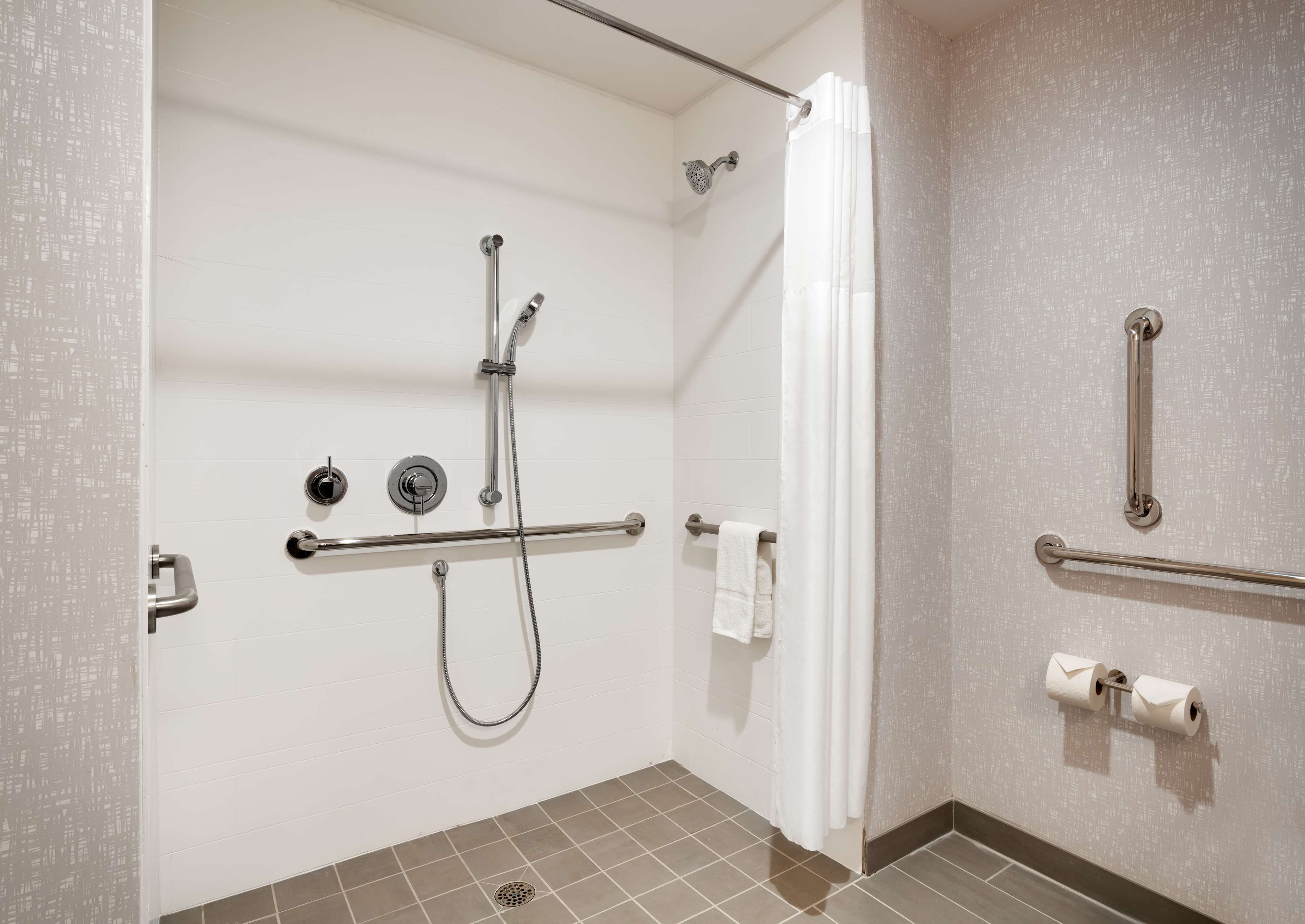 A bathroom with a shower, grab bars, a towel rack, and a toilet paper holder.