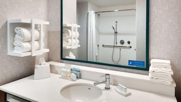 Une salle de bain moderne avec un grand miroir, un lavabo et une douche. On y trouve également des porte-serviettes et un distributeur de savon sur le comptoir.