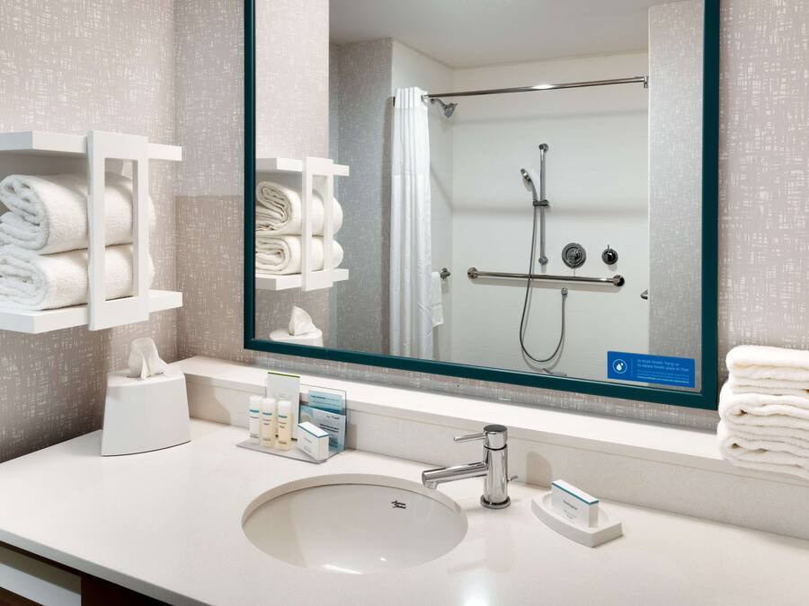Une salle de bain moderne avec un grand miroir, un lavabo et une douche. On y trouve également des porte-serviettes et un distributeur de savon sur le comptoir.