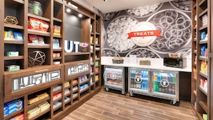 A snack and treat section with shelves stocked with various snacks, a refrigerated display case, and a microwave on a counter. - Hampton Inn Draper Salt Lake City Ut (Draper)