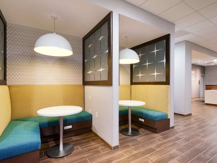 A modern waiting area with cushioned seating and round tables, featuring geometric wall patterns and recessed lighting.