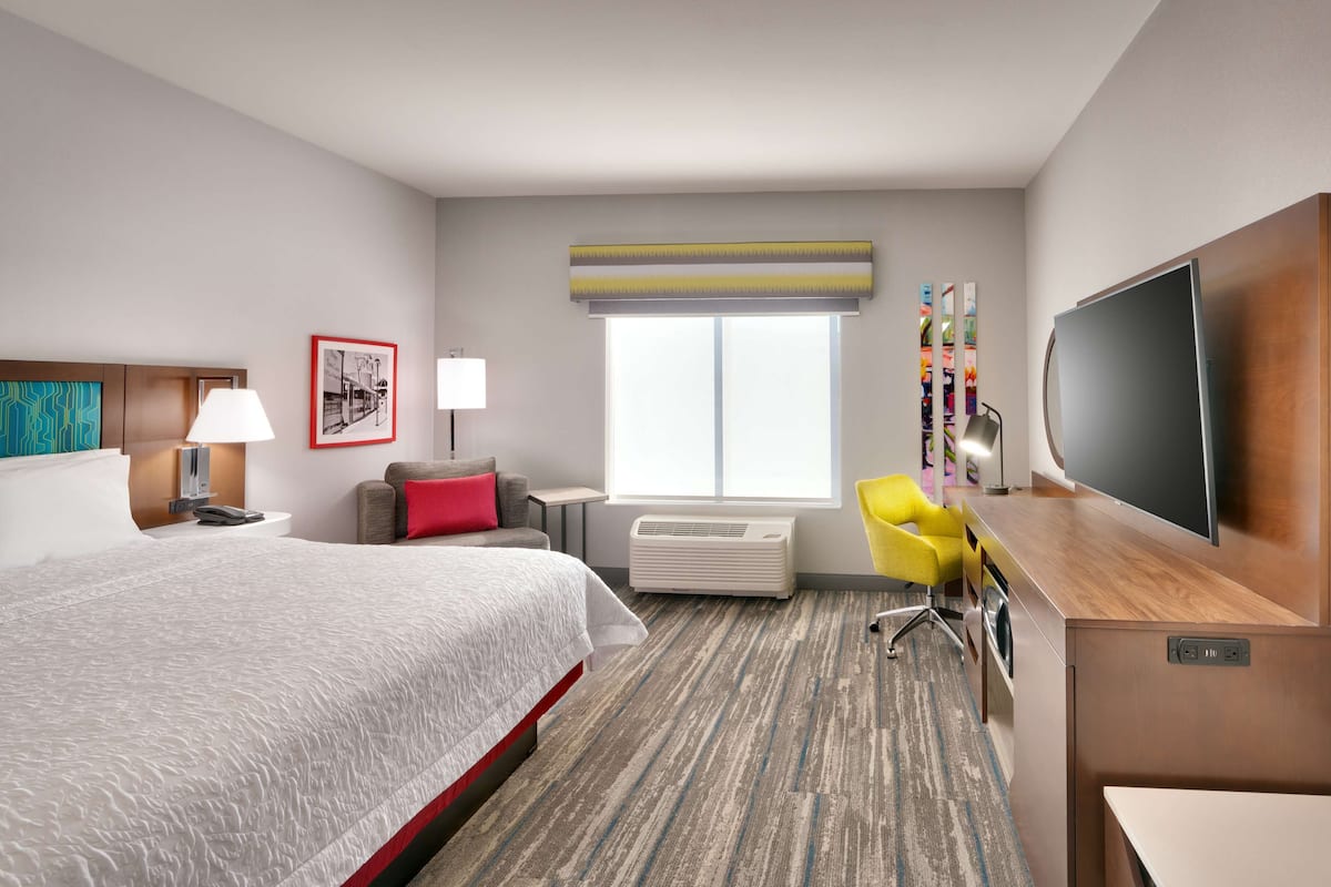 A hotel room with a bed, a desk, a chair, a television, and a window.