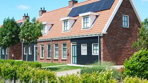 Una casa de dos pisos con techo inclinado, paneles solares y fachada de ladrillo.
