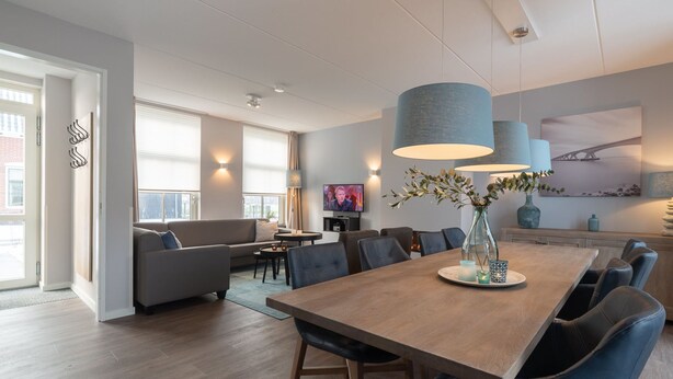 Un comedor moderno con una mesa de madera, sillas tapizadas en azul y un jarrón con ramas.