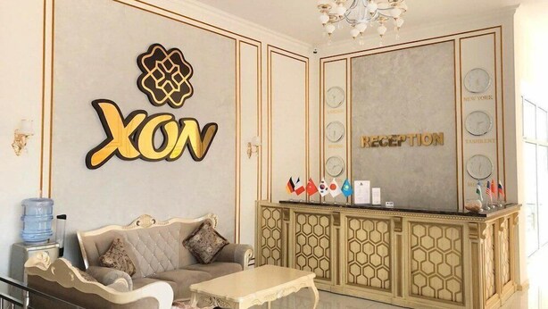 A reception area with a 'XON' sign, a reception desk, and a seating area with a sofa and coffee table. - Reikartz Xon Tashkent (Tashkent)