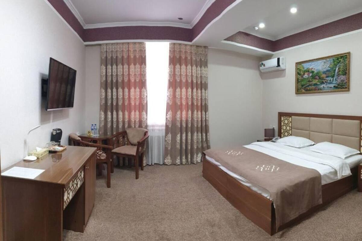 A hotel room with a bed, a desk, a chair, a TV, and curtains.