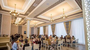 A large dining hall with multiple tables and chairs, ornate ceiling designs, and chandeliers. - Reikartz Xon Tashkent (Tashkent)