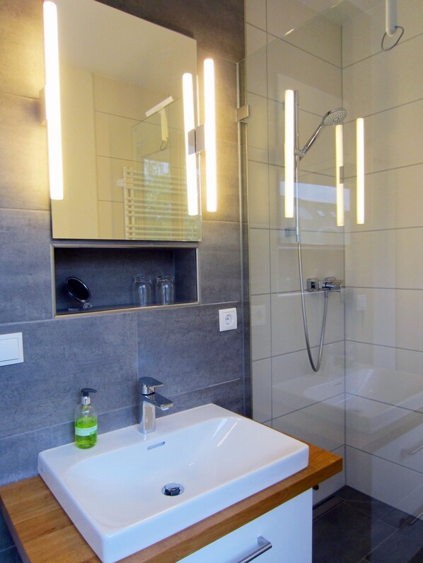 Une salle de bain moderne avec un lavabo blanc, un miroir et une douche.