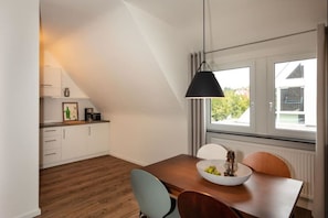 Une cuisine moderne avec des meubles blancs, une table à manger en bois et un luminaire suspendu noir.