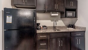 A compact kitchen with dark wood cabinets, a black refrigerator, a microwave, and a granite countertop.