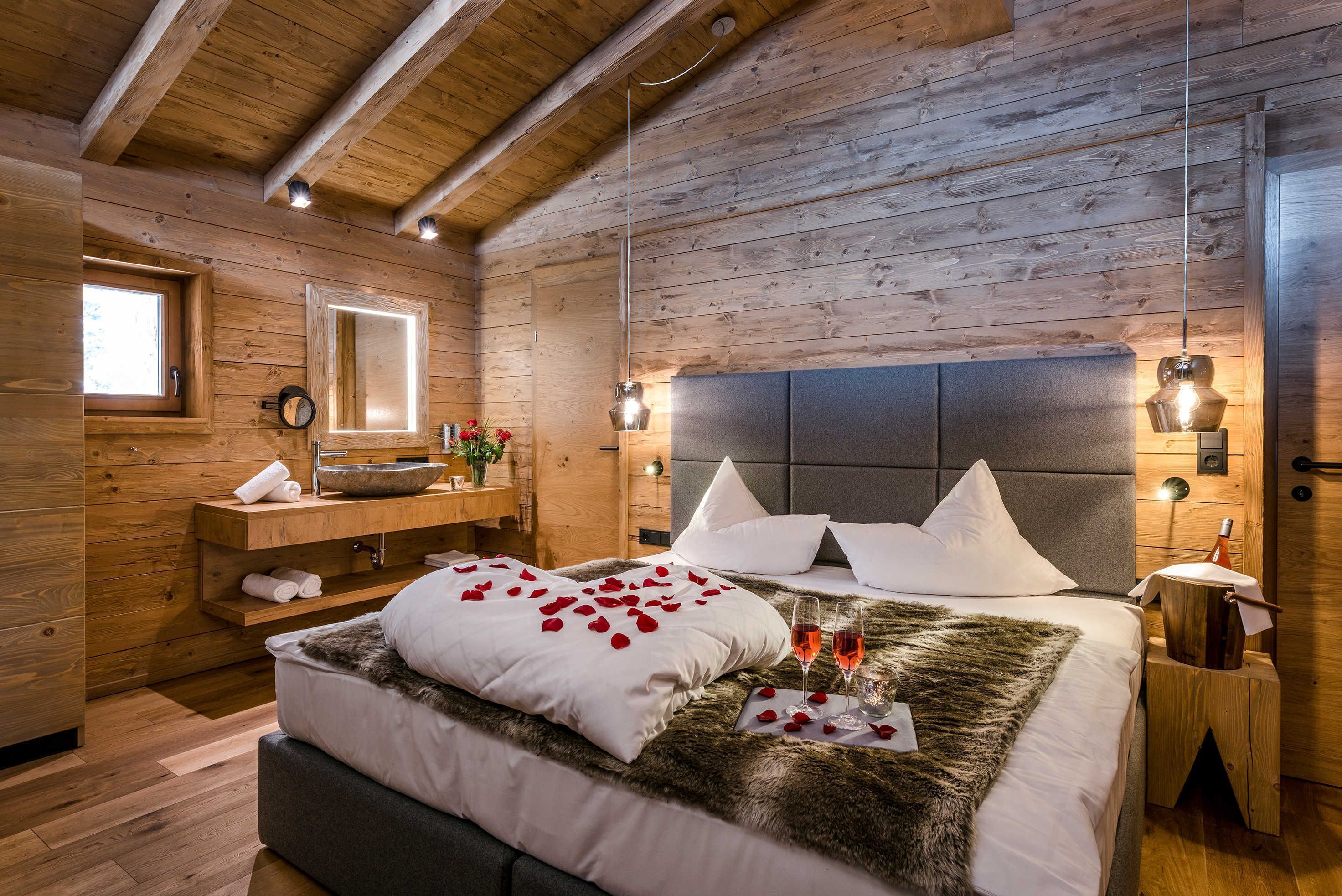 Een slaapkamer in een houten hutje, met een bed, nachtkastjes, een spiegel en een raam.