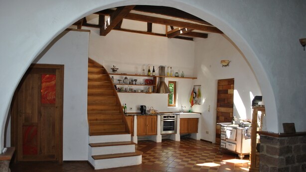 A kitchen with a wooden staircase, a stone fireplace, and a tiled floor.