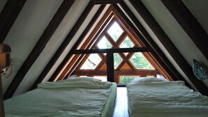 A room with two beds, a wooden ceiling, and a large window with a view of trees.