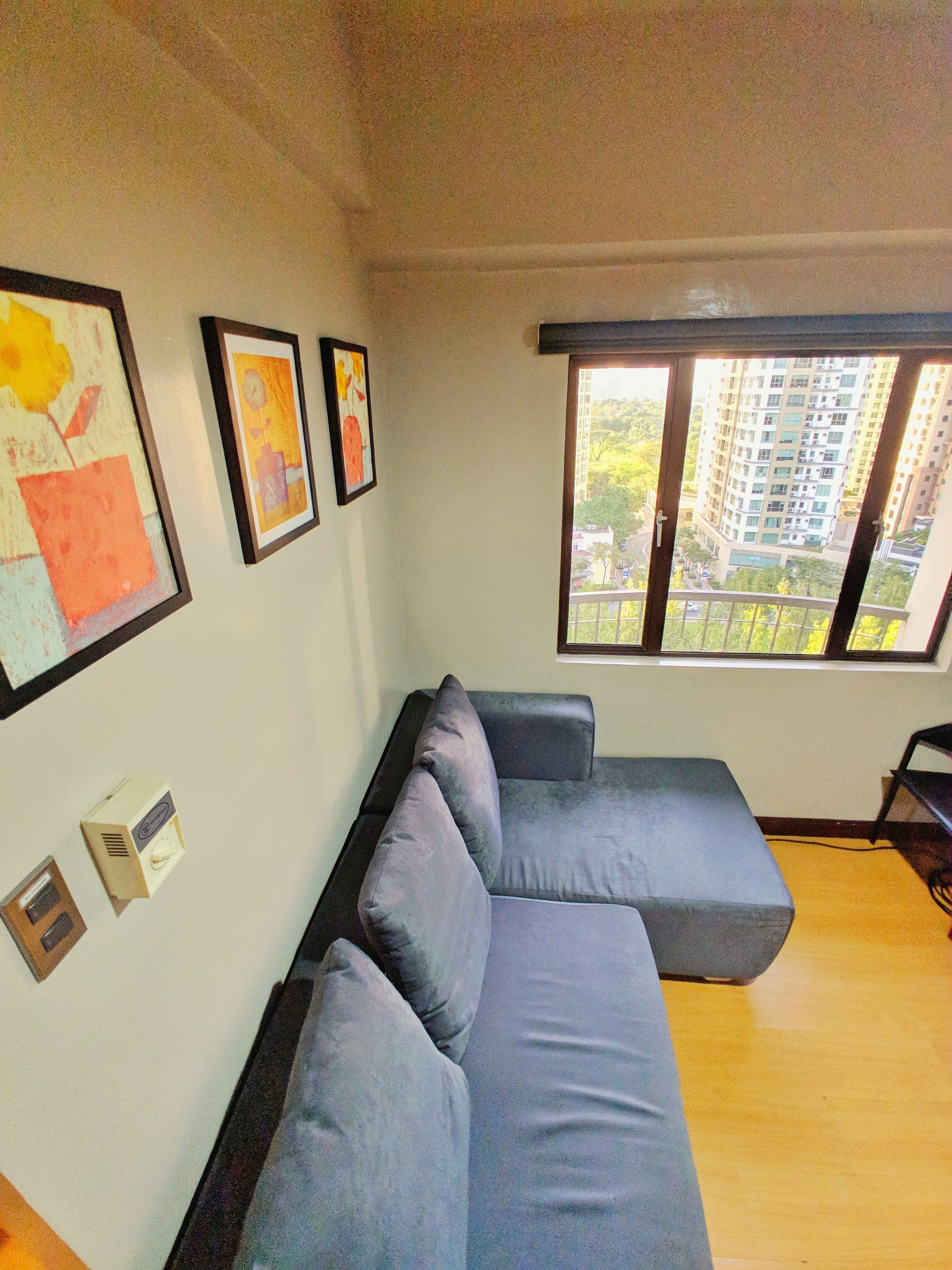 Un salón moderno con un sofá seccional gris, un ventanal con vistas a un paisaje urbano y cuadros en la pared.