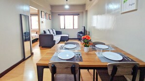 Un coin repas avec une table en bois dressée pour quatre personnes, un canapé et un téléviseur en arrière-plan.
