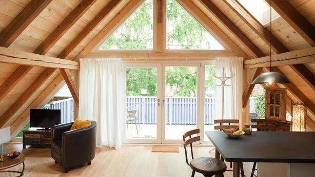 A spacious attic room with a large window, wooden beams, a television, a sofa, and a dining table. - Living in a unique atmosphere near the Europapark Rust (Ettenheim)