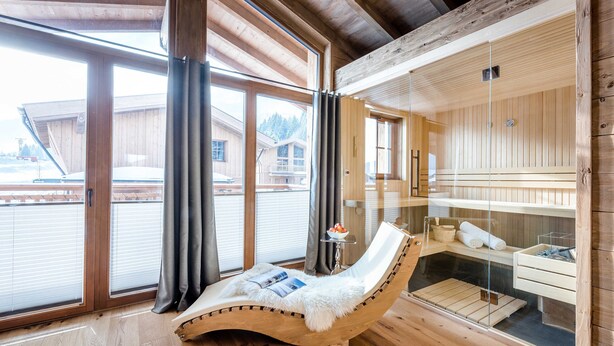Een houten interieur met een sauna in glazen afsluiting, een ligstoel met een tijdschrift en een houten vloer.